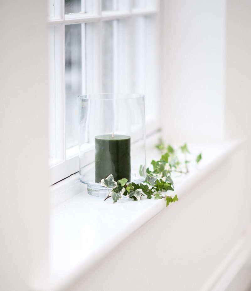 A beautiful vertical shot of a black candle in a glass decorated with leaves on a window shelf
